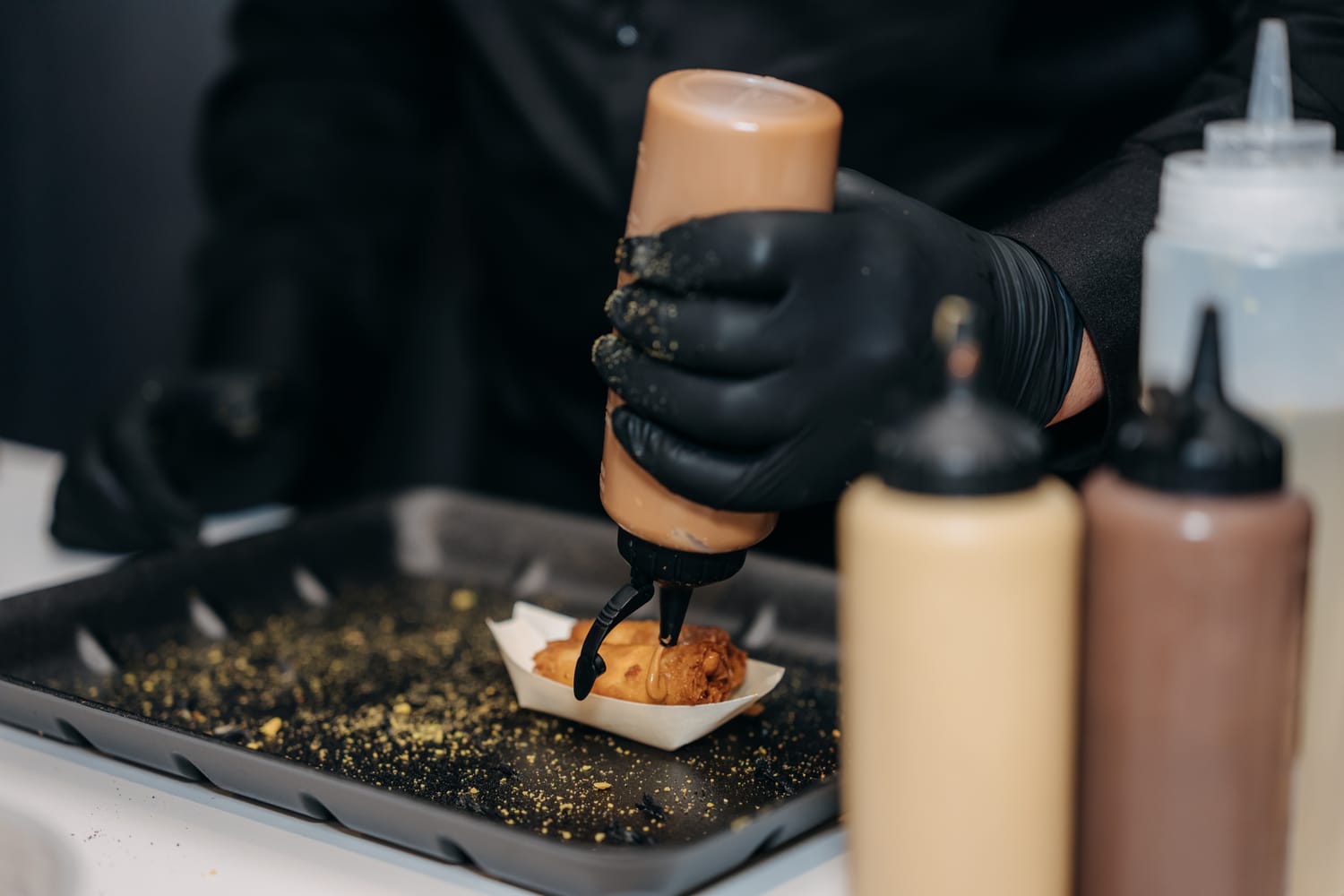 A gloved hand finishing a znood el sit with sauce at the live station.